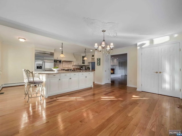 kitchen featuring white cabinetry, light hardwood / wood-style floors, decorative light fixtures, a kitchen island with sink, and appliances with stainless steel finishes