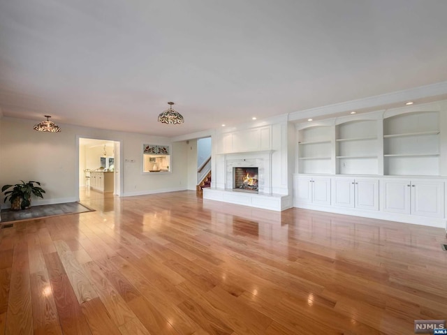 unfurnished living room with built in features and light hardwood / wood-style flooring