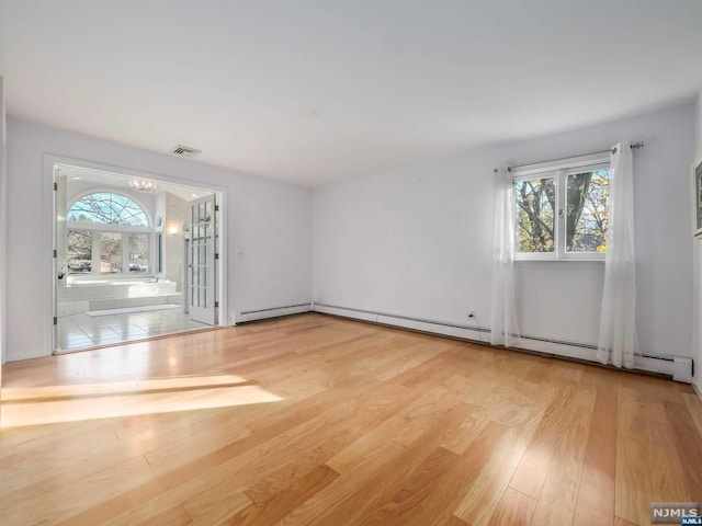 spare room with a notable chandelier, baseboard heating, and light hardwood / wood-style flooring