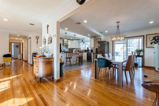 dining area featuring crown molding, light hardwood / wood-style flooring, beverage cooler, and an inviting chandelier