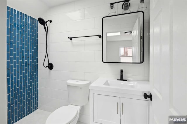 bathroom featuring tile walls, a tile shower, vanity, and toilet