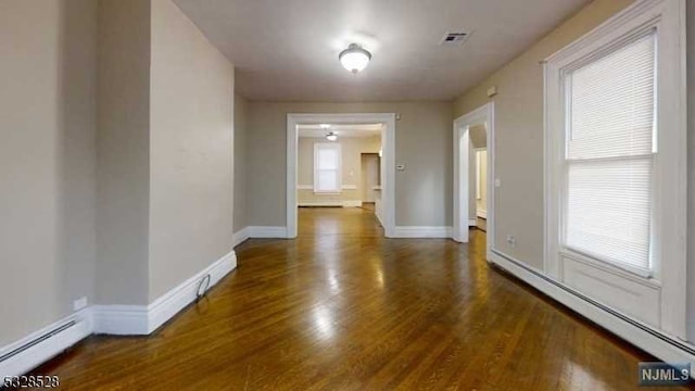 spare room featuring baseboard heating and dark wood-type flooring