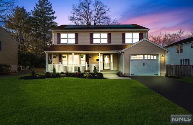 view of front of home featuring a lawn, covered porch, a garage, and solar panels