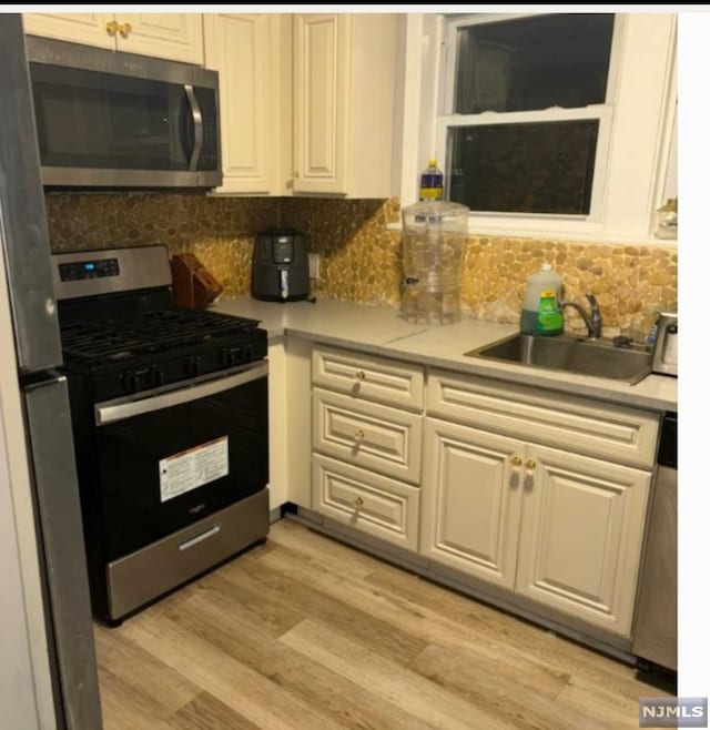 kitchen featuring decorative backsplash, sink, stainless steel appliances, and light hardwood / wood-style flooring