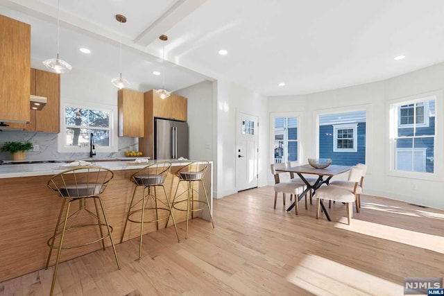 kitchen with pendant lighting, a kitchen breakfast bar, decorative backsplash, light wood-type flooring, and stainless steel refrigerator