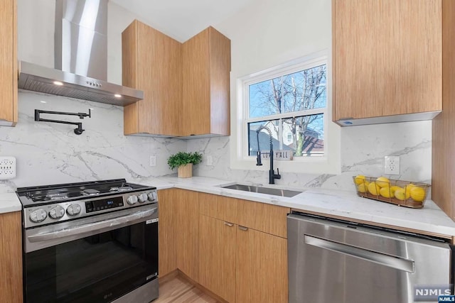 kitchen with wall chimney range hood, sink, decorative backsplash, light stone countertops, and appliances with stainless steel finishes