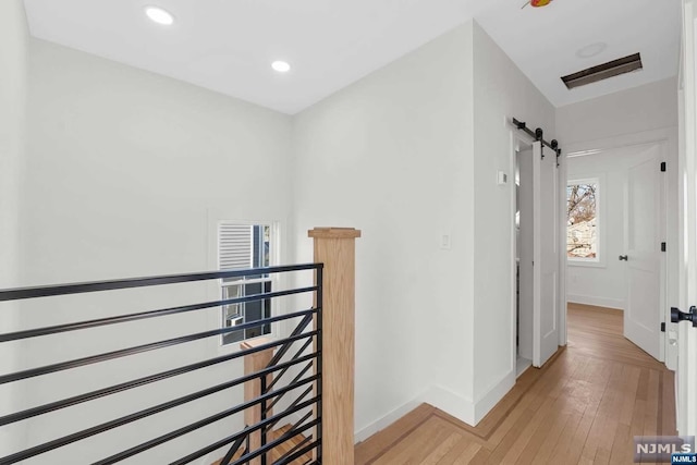 hall with a barn door and light hardwood / wood-style floors