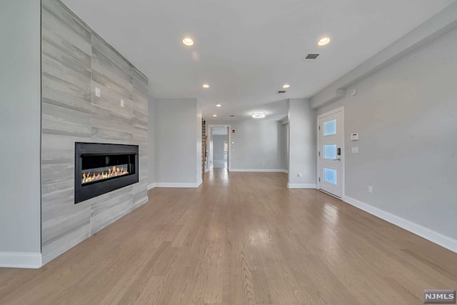 unfurnished living room with a tiled fireplace and light hardwood / wood-style flooring