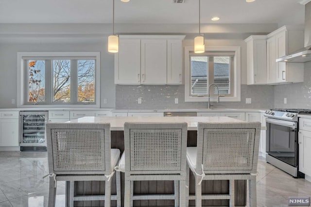 kitchen featuring wine cooler, stainless steel range, wall chimney range hood, white cabinetry, and hanging light fixtures