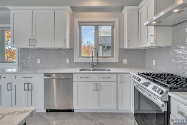 kitchen with white cabinets, sink, wall chimney exhaust hood, appliances with stainless steel finishes, and tasteful backsplash