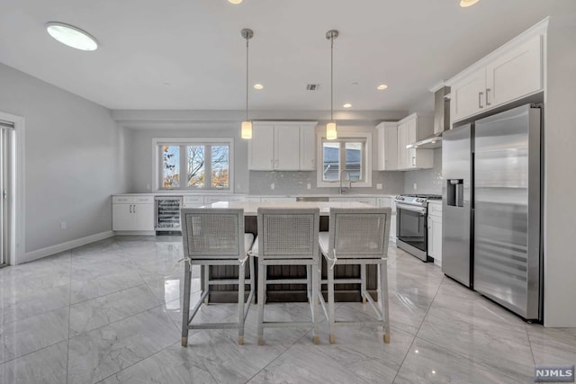 kitchen with a center island, wall chimney exhaust hood, a wealth of natural light, decorative light fixtures, and stainless steel appliances