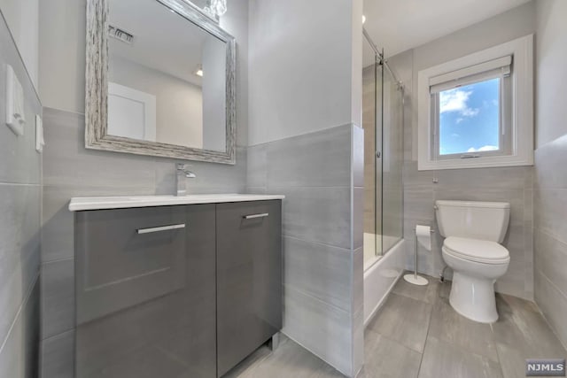 full bathroom with vanity, bath / shower combo with glass door, tile walls, and toilet