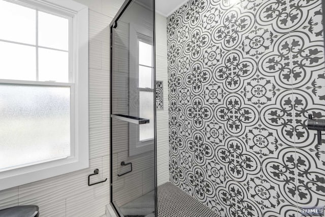 bathroom with a shower with door, a healthy amount of sunlight, and tile walls