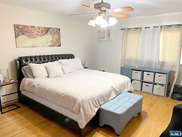 bedroom with a wall unit AC, ceiling fan, a baseboard radiator, and hardwood / wood-style flooring