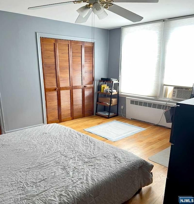 bedroom featuring a closet, ceiling fan, radiator heating unit, and wood-type flooring