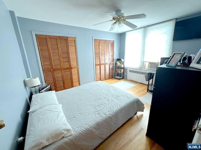 bedroom featuring light wood-type flooring, radiator, multiple closets, and ceiling fan