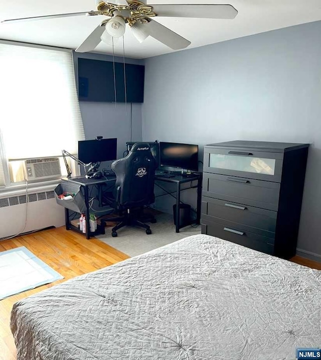 bedroom featuring radiator, hardwood / wood-style flooring, ceiling fan, and cooling unit