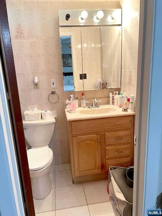 bathroom featuring toilet, vanity, tile patterned floors, and tile walls