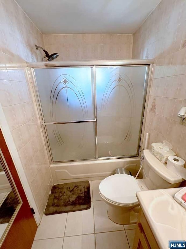 full bathroom with tile patterned floors, bath / shower combo with glass door, vanity, tile walls, and toilet