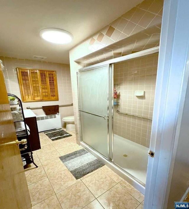 bathroom featuring a shower with door, radiator, tile patterned floors, toilet, and tile walls