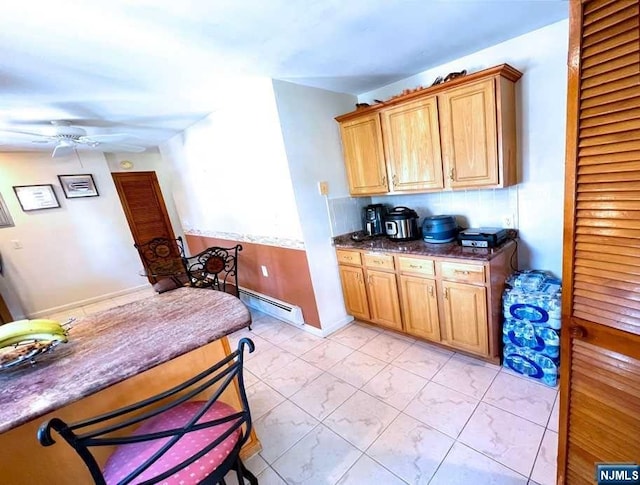 kitchen with ceiling fan, baseboard heating, and dark stone counters