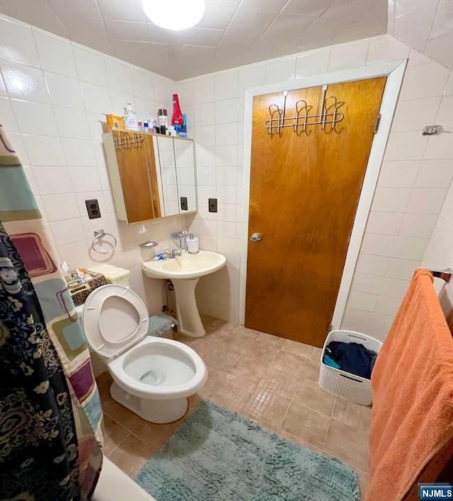 bathroom featuring toilet, tile patterned floors, tile walls, and sink