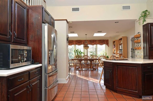 kitchen with tile patterned floors, kitchen peninsula, pendant lighting, dark brown cabinets, and appliances with stainless steel finishes