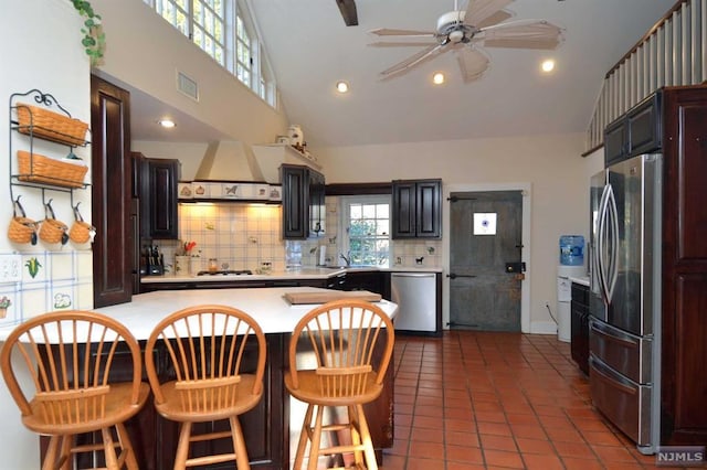 kitchen with decorative backsplash, appliances with stainless steel finishes, custom exhaust hood, dark tile patterned floors, and high vaulted ceiling