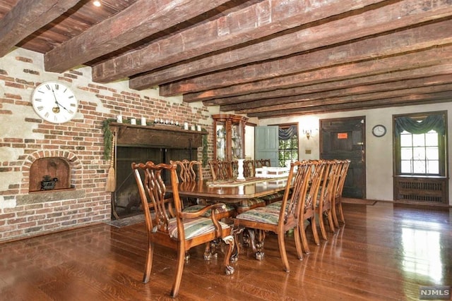 dining room with a fireplace, beam ceiling, dark wood-type flooring, and brick wall