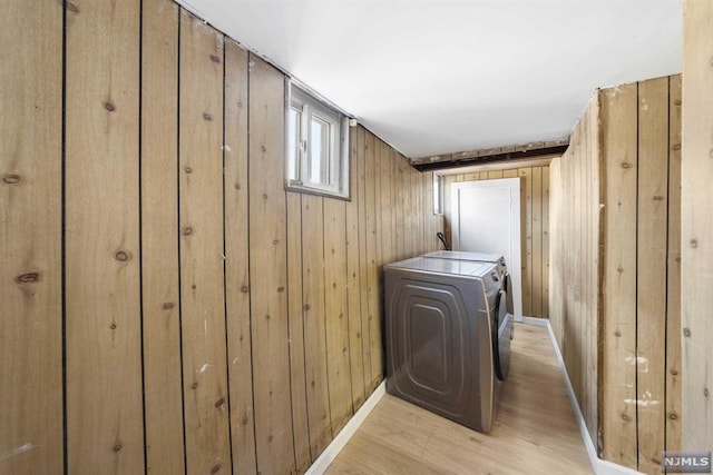 clothes washing area with washer and dryer, light wood-type flooring, and wooden walls