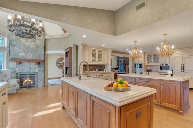 kitchen with a large island with sink, a high ceiling, a stone fireplace, hanging light fixtures, and light wood-type flooring