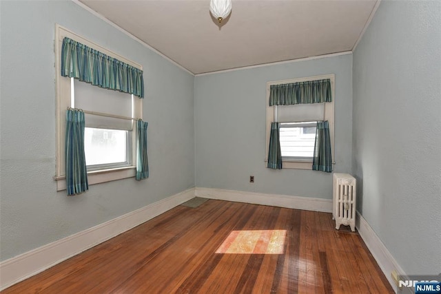 empty room with radiator heating unit, hardwood / wood-style flooring, and crown molding