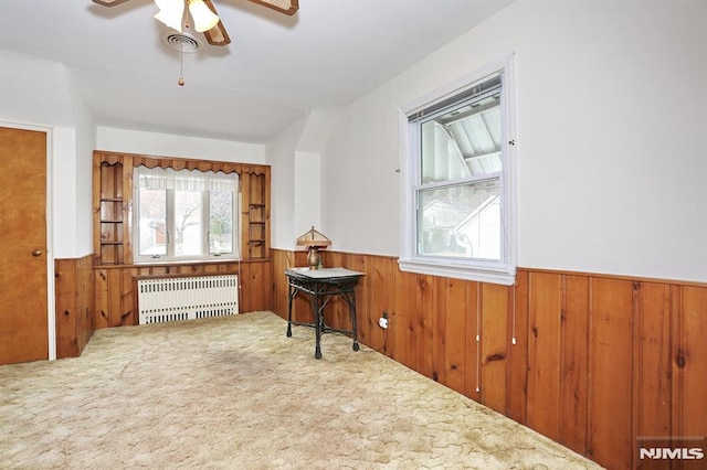 interior space with carpet flooring, radiator heating unit, ceiling fan, and wood walls