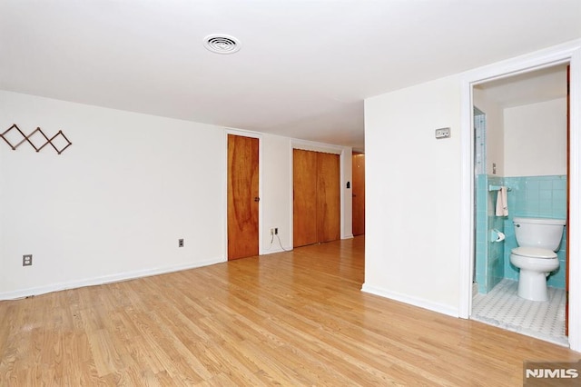 spare room featuring tile walls and light hardwood / wood-style flooring