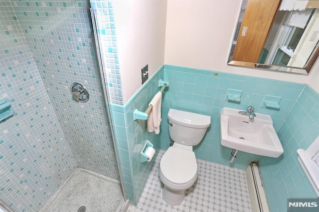 bathroom with tile walls, tiled shower, sink, and toilet