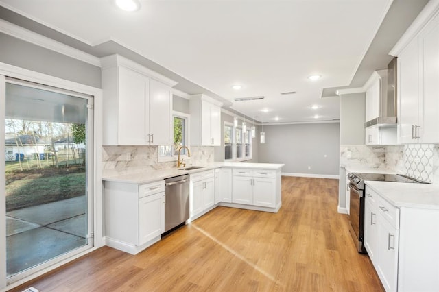 kitchen with sink, wall chimney range hood, light hardwood / wood-style flooring, white cabinets, and appliances with stainless steel finishes