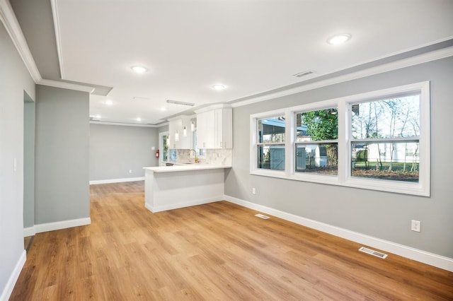 kitchen with light hardwood / wood-style floors, white cabinetry, kitchen peninsula, and crown molding