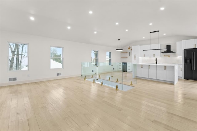 unfurnished living room with sink, light hardwood / wood-style floors, and vaulted ceiling