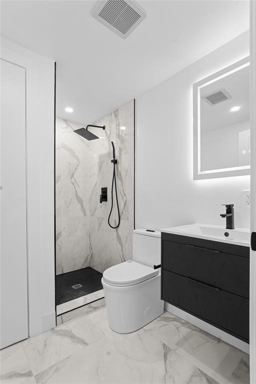 bathroom with a tile shower, vanity, and toilet