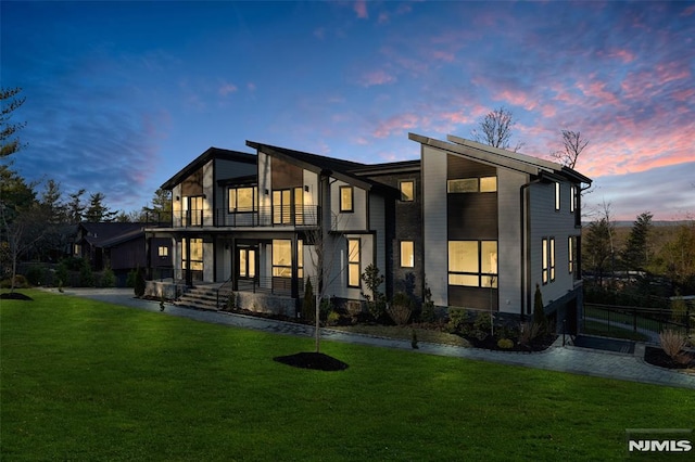 back house at dusk with a lawn and a balcony