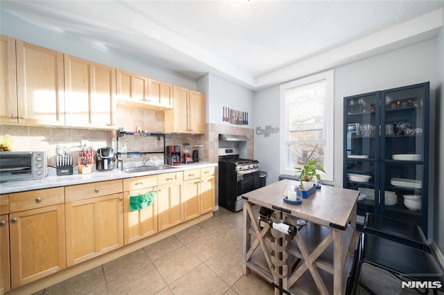 kitchen with decorative backsplash, stainless steel gas range oven, sink, and light brown cabinetry