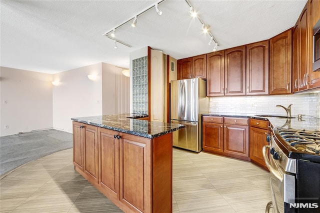 kitchen featuring a center island, sink, stainless steel appliances, backsplash, and dark stone countertops