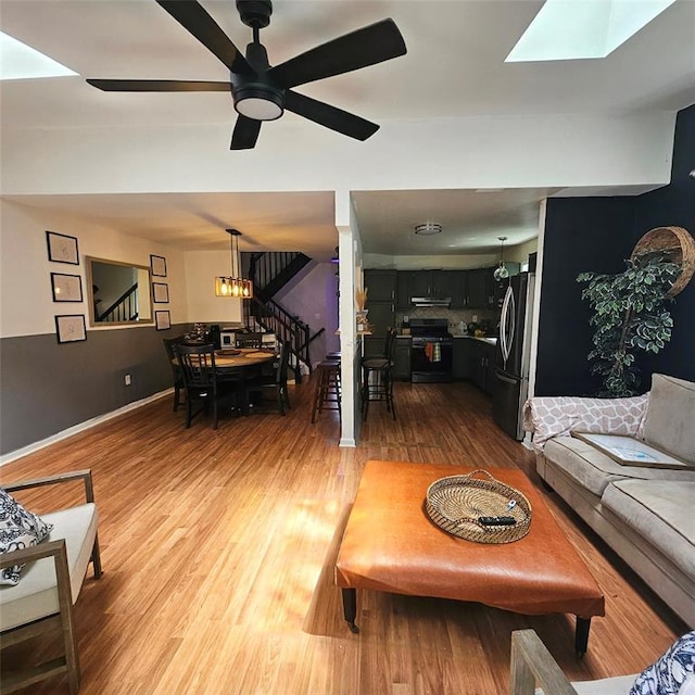 living room featuring hardwood / wood-style flooring, ceiling fan with notable chandelier, and a skylight