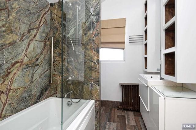 bathroom with radiator heating unit, vanity, tiled shower / bath combo, and hardwood / wood-style flooring