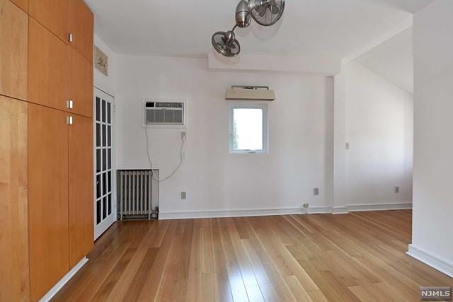 spare room featuring radiator heating unit, light wood-type flooring, and a wall mounted AC