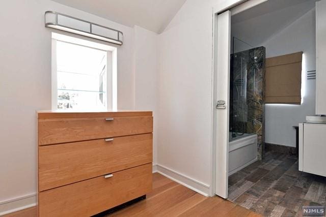 bathroom with vanity, hardwood / wood-style flooring, vaulted ceiling, and tub / shower combination