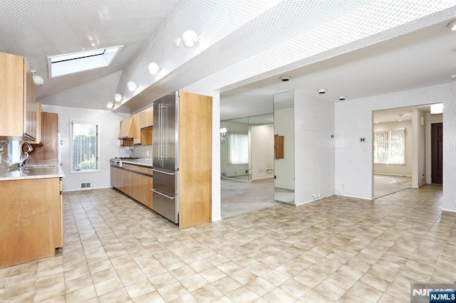 kitchen featuring vaulted ceiling with skylight, sink, high quality fridge, and a wealth of natural light