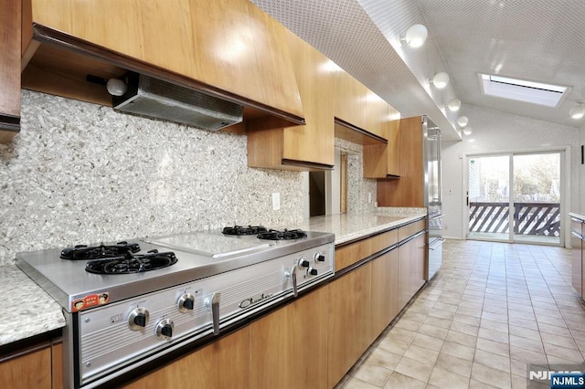 kitchen with vaulted ceiling with skylight, backsplash, stainless steel gas cooktop, light tile patterned floors, and wall chimney exhaust hood