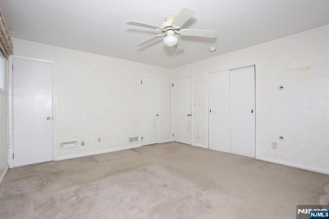 unfurnished bedroom with multiple closets, ceiling fan, and light carpet