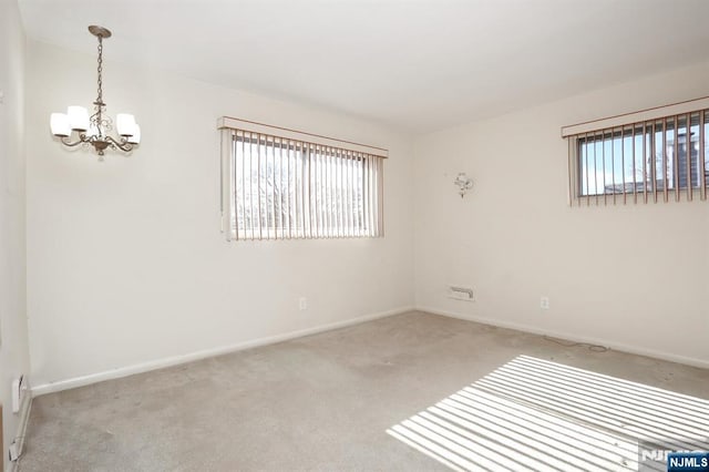 spare room featuring plenty of natural light, light carpet, and an inviting chandelier